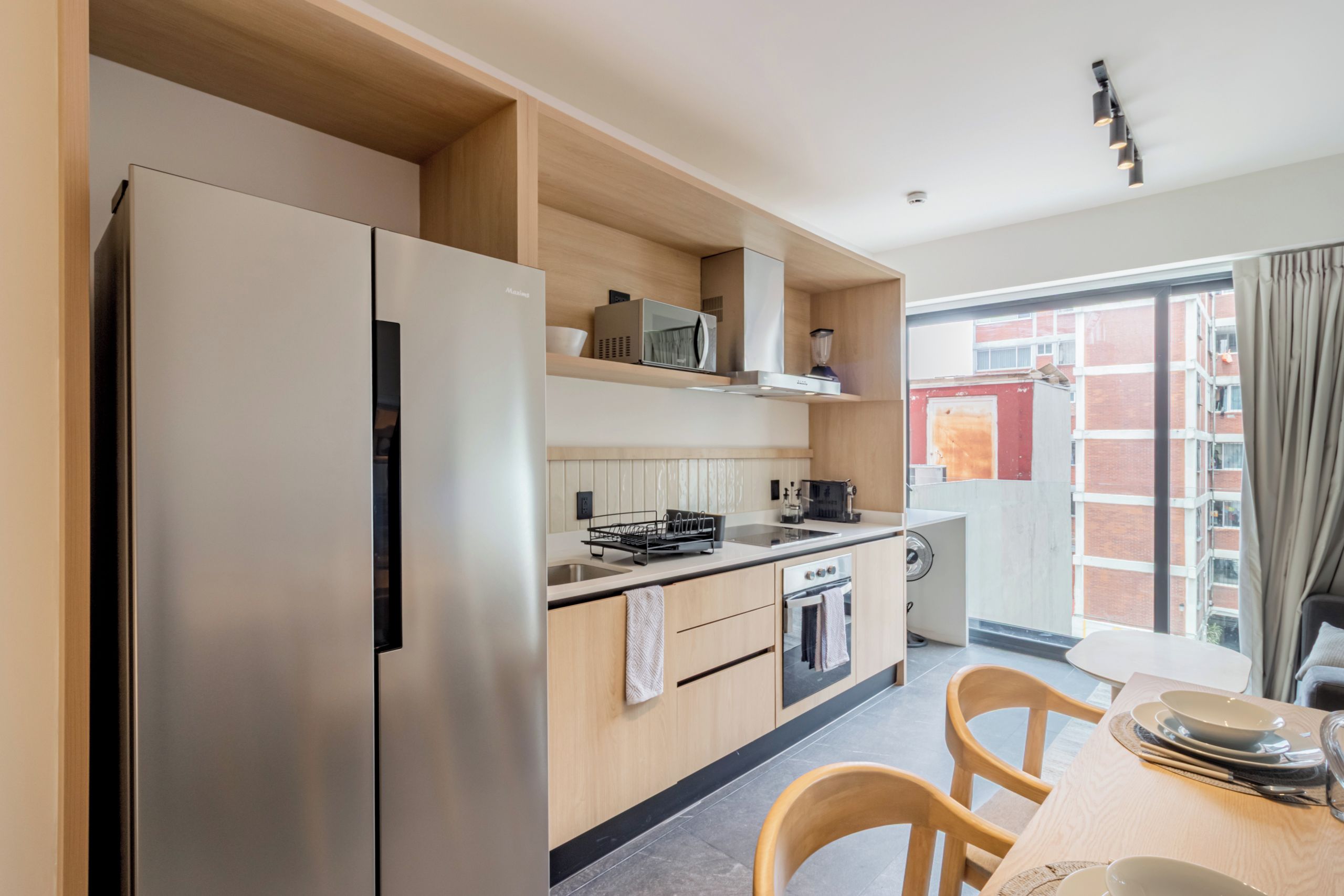 A modern kitchen with a refrigerator, microwave, oven, and sink. There is a dining area with a table and chairs.