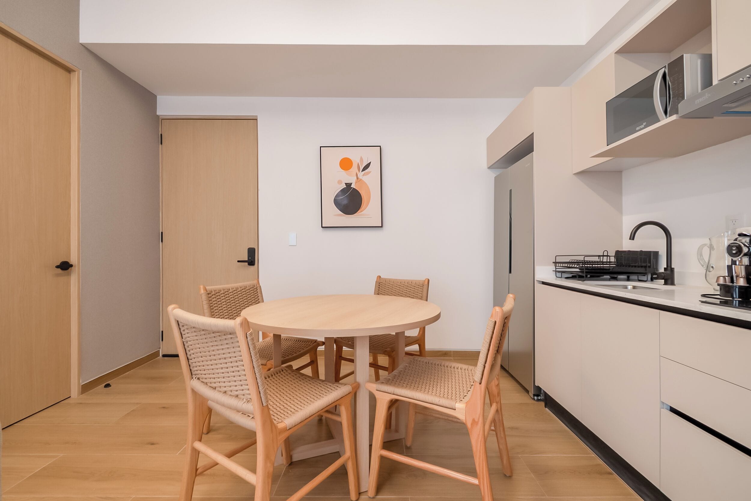 A compact kitchen with a dining area, featuring a round wooden table and wicker chairs.