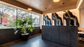 Una moderna zona de recepción con una planta grande en maceta, un mostrador de recepción y vistas al exterior.