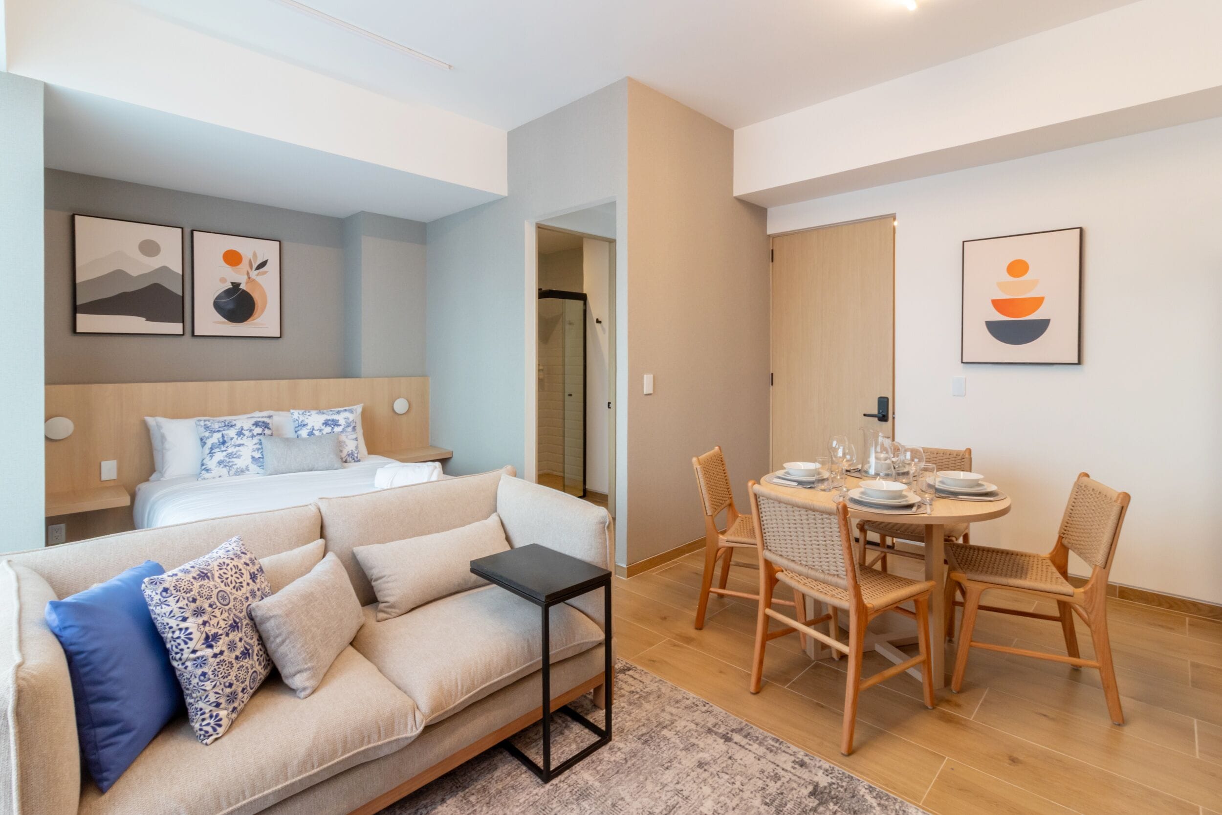 Una habitación de hotel moderna con cama, sofá, mesa de comedor con sillas y obras de arte en las paredes.