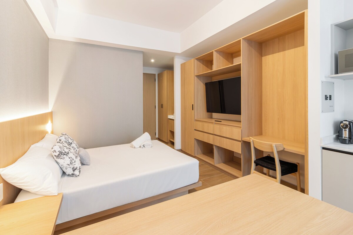 A modern hotel room with a bed, a desk, a television, and built-in storage.