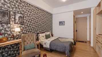 Un dormitorio con cama, una silla, un escritorio con lámpara y un papel tapiz floral en la pared.