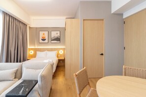 A hotel room with a bed, two sofas, a dining table, and a chair. There are two wall-mounted lights and two framed pictures above the bed.