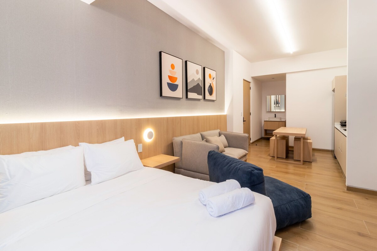A hotel room with a bed, a sofa, a desk, and a mirror.