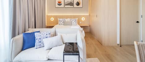 A modern hotel room with a bed, a sofa, a small table, and artwork on the wall.