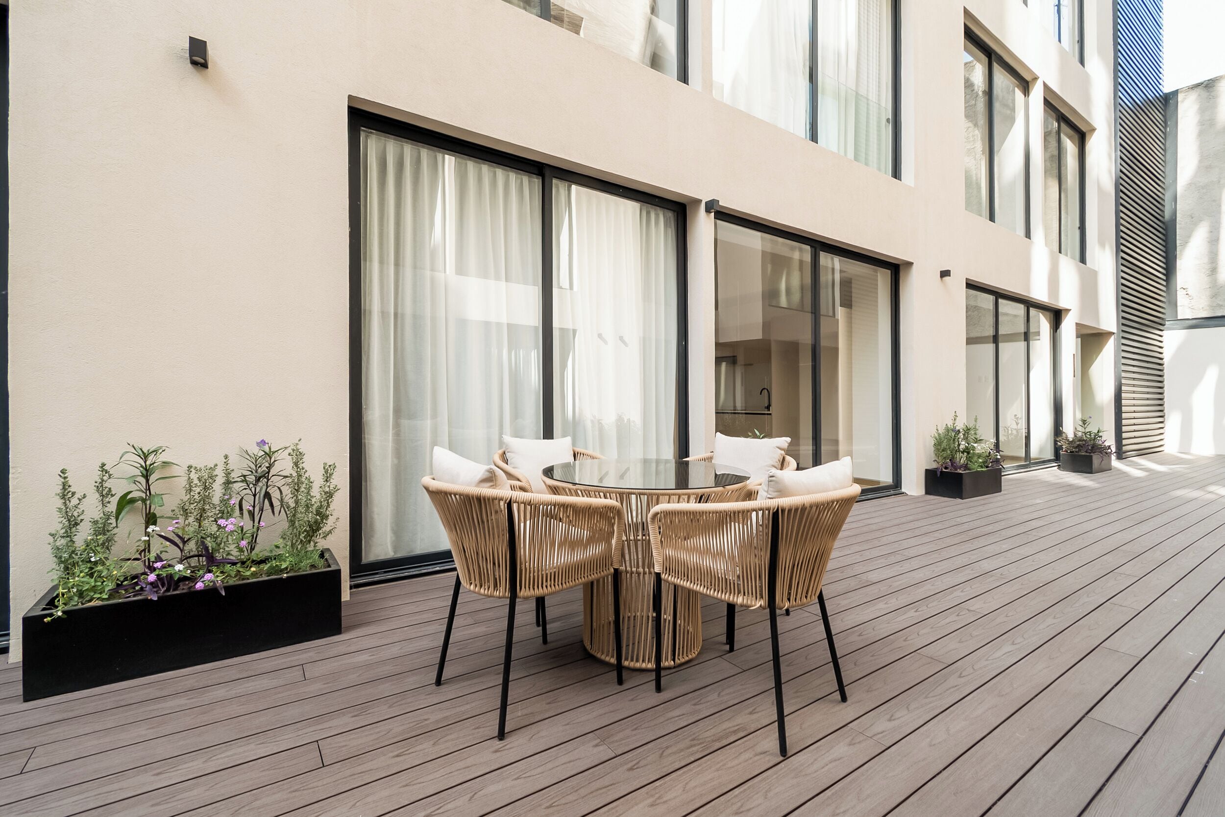 An outdoor patio with a round table and wicker chairs, a wooden deck, and potted plants.