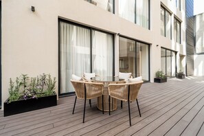 An outdoor patio with a round table and wicker chairs, a wooden deck, and potted plants.