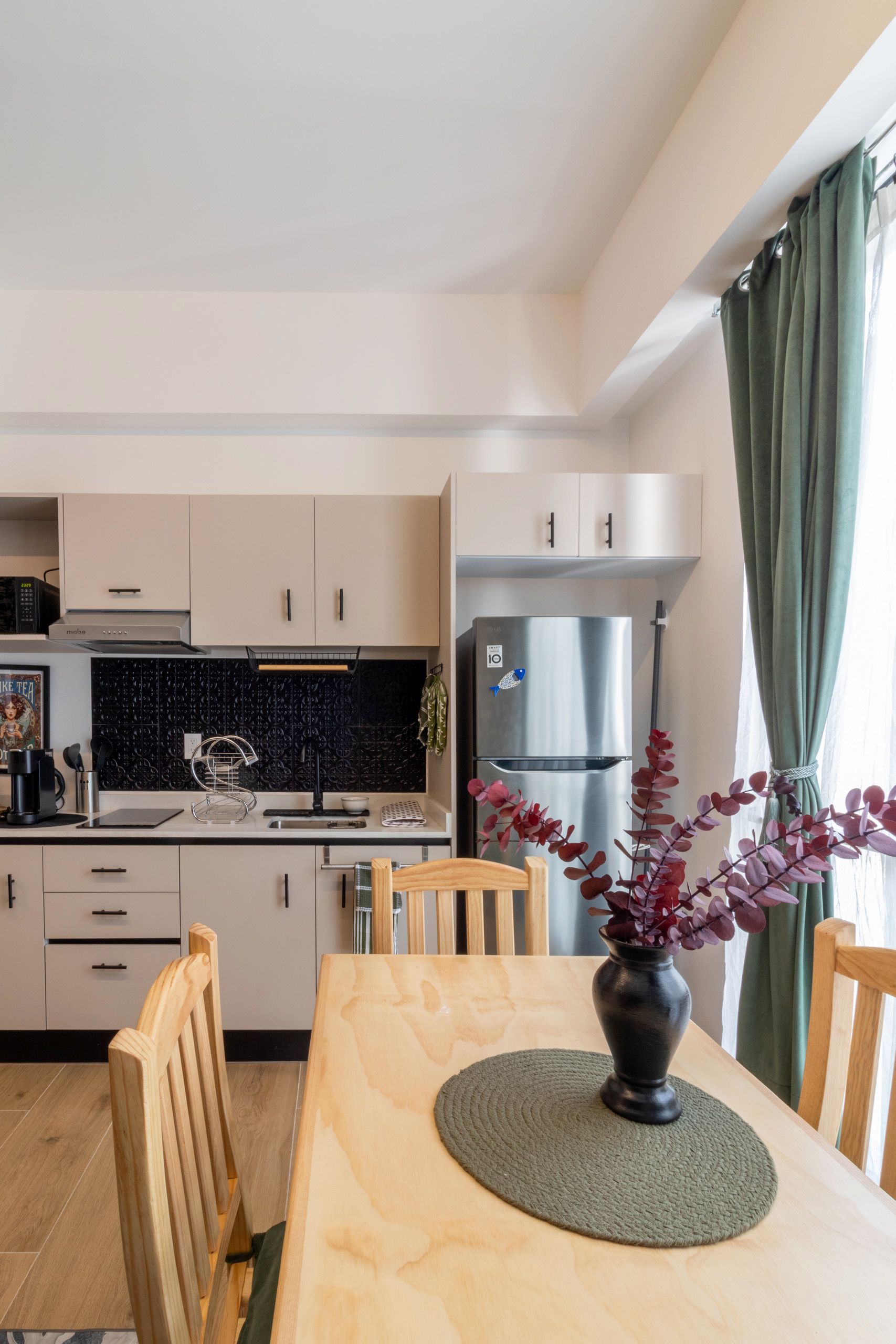 A modern kitchen with light-colored cabinets, a stainless steel refrigerator, and a dining table with chairs.