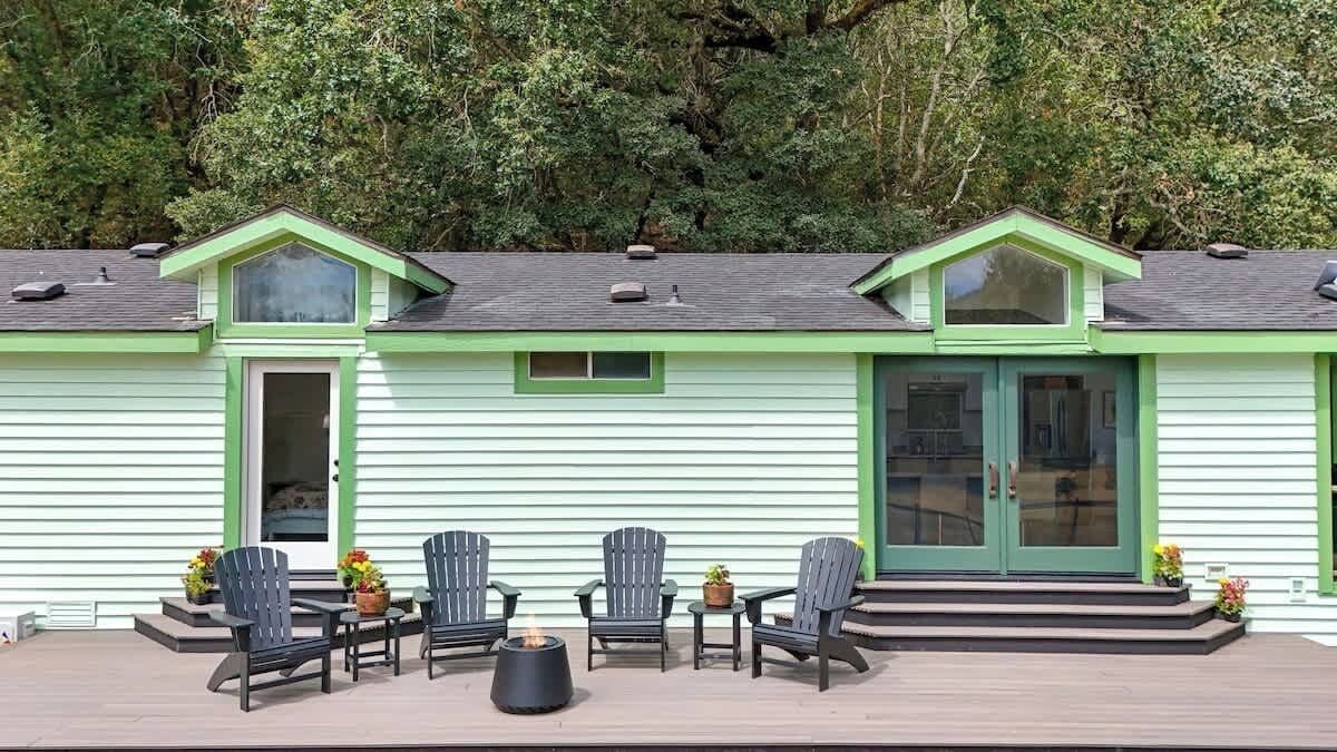 A house with a green exterior, a covered porch with Adirondack chairs, and a fire pit.
