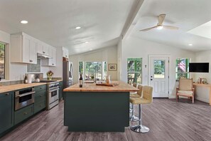 A spacious kitchen with a central island, stainless steel appliances, and a ceiling fan. - Maple Ring Kenwood Cottage (Kenwood)
