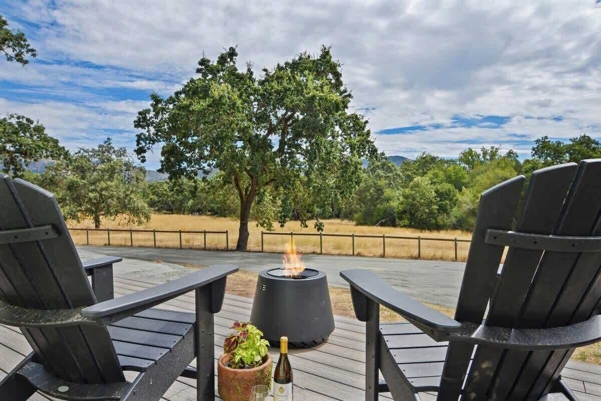 Eine Terrasse mit zwei Stühlen und einem Feuerkorb, umgeben von Bäumen und Blick auf die Landschaft.