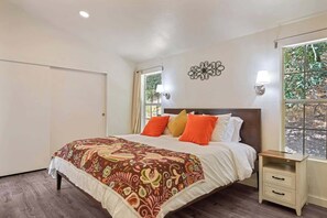 A bedroom with a bed, bedside tables, a window, and a door. - Maple Ring Kenwood Cottage (Kenwood)