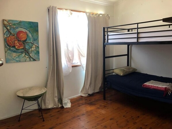 A room with a bunk bed, a small stool, a painting, and a window with curtains.