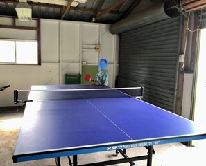 A ping pong table with a net, a green chair, and a closed door in the background.