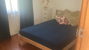 Ein Einzelbett mit Holzbettgestell und dunkelblauer Matratze in einem Zimmer mit Holzboden.