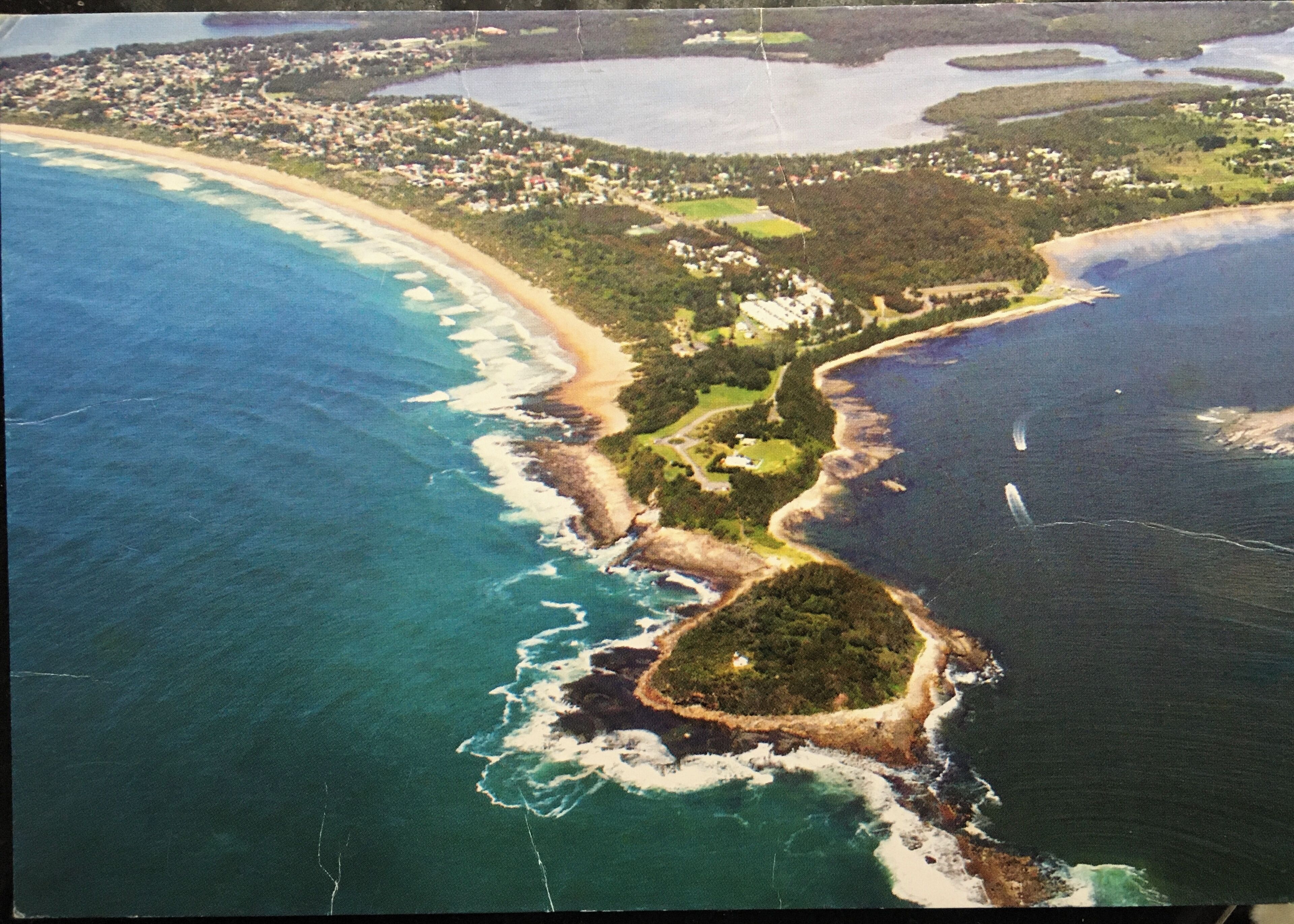 Una vista aerea di una zona costiera con spiaggia, una piccola isola e un'area residenziale.