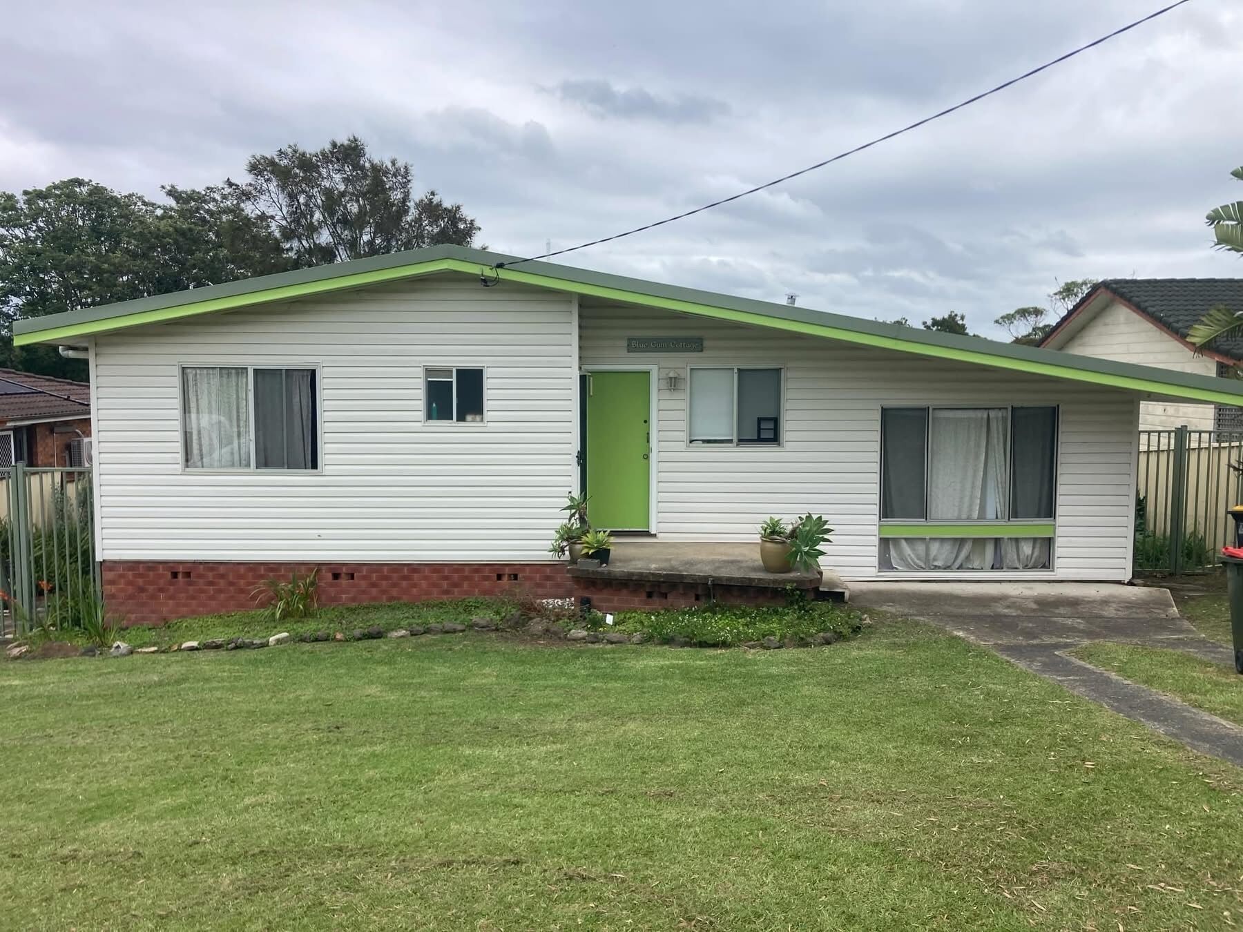 A single-story mobile home with a green door, a small porch with potted plants, and a grassy yard.
