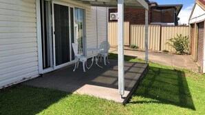 Eine überdachte Terrasse mit Tisch und St ühlen, eine Schiebetür und eine Ziegelwand im Hintergrund.