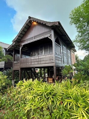 A traditional wooden house with a balcony, surrounded by lush greenery.