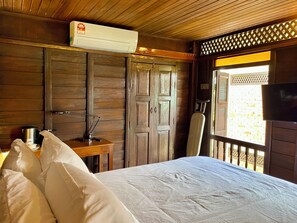 Una habitación de madera con una cama, un escritorio con una lámpara, un equipo de aire acondicionado y un televisor.
