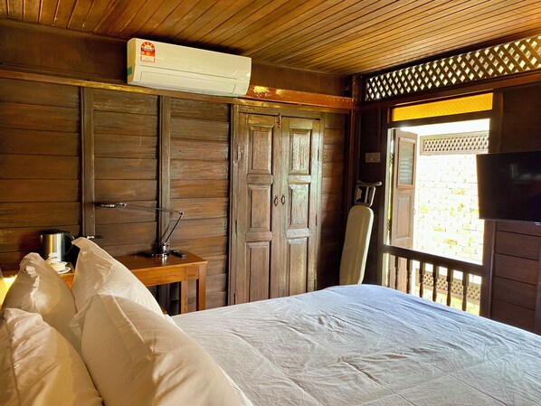 A wooden room with a bed, a desk with a lamp, an air conditioning unit, and a television.