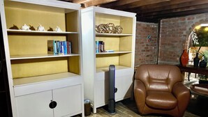 Ein Zimmer mit einem braunen Ledersessel, weißen Regaleinheiten mit Büchern und Dekoration sowie einem Teppich mit Muster.