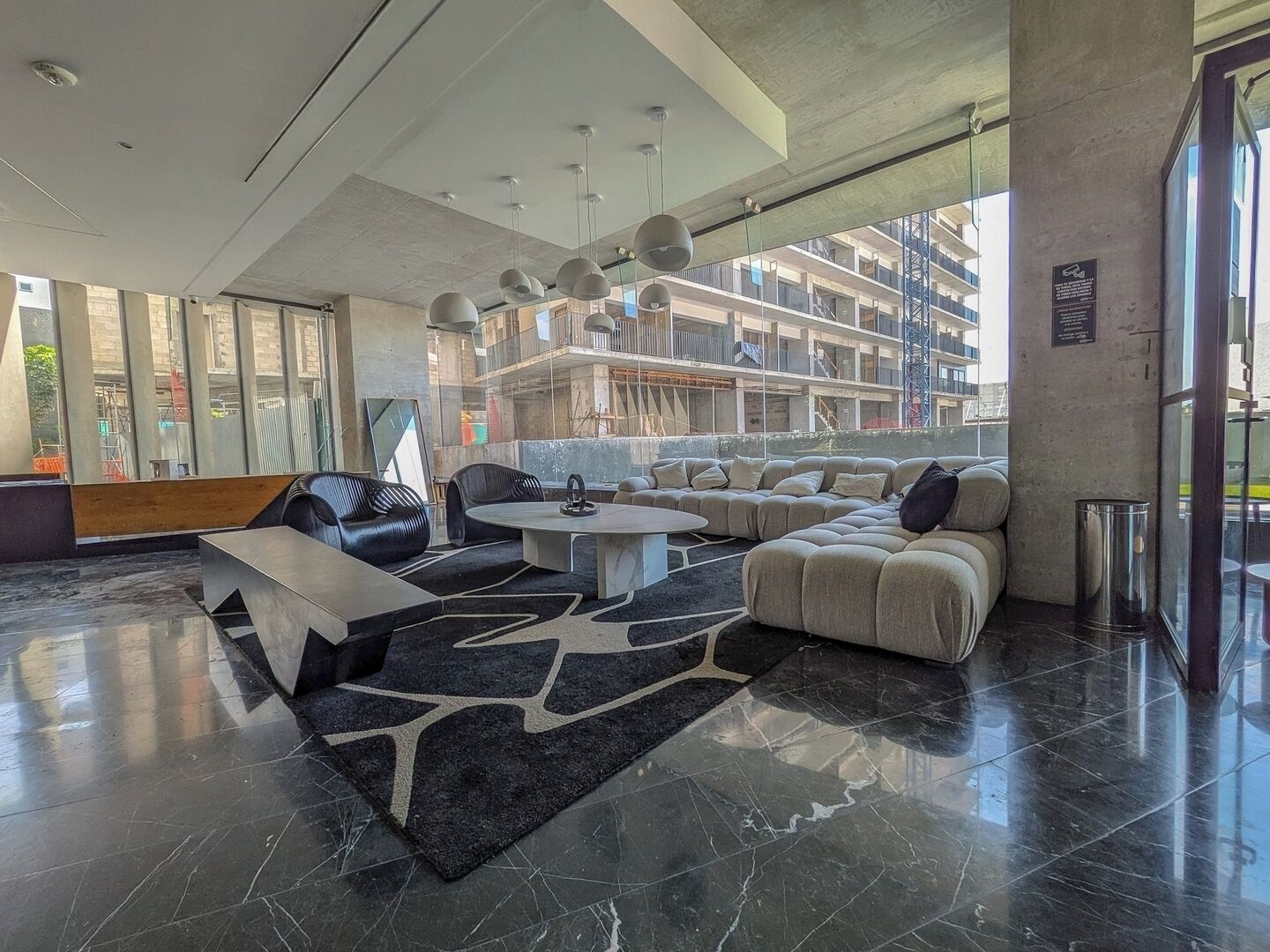 Un hall d’entrée moderne doté d’un espace salon, d’une table basse et d’une grande fenêtre offrant une vue sur la façade de l’immeuble.