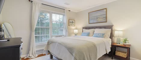A bedroom with a bed, bedside tables, a lamp, a painting, and a window with curtains.