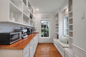 A kitchen with white cabinetry, a coffee machine, and a window with a view of greenery. - La Belle Vie 
Hot Tub • Fire Pit • Outdoor Kitchen • Sleeps 12 (Lake Ariel)