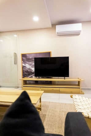 A modern living room with a flat-screen TV on a wooden stand, a glass door with a time display, and a patterned rug on the floor. - Unwind in Guadalajara | Torre Villadhara (Guadalajara)