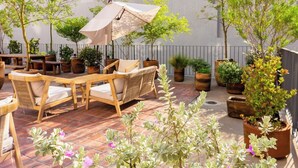 Eine Terrasse im Freien mit Holzmöbeln, Blumentöpfen und einem großen Sonnenschirm.