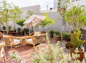 An outdoor patio with wooden furniture, potted plants, and a large umbrella. - Unwind in Guadalajara | Torre Villadhara (Guadalajara)