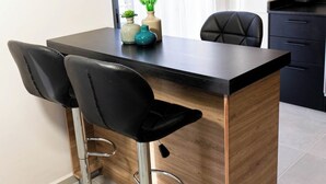 Eine moderne Küche mit einer Holztischinsel, zwei schwarzen Barhocker und einem Mixer auf der Arbeitsfläche.