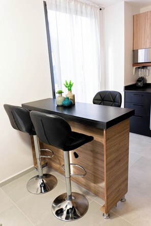 A modern kitchen with a wooden island, two black bar stools, and a blender on the countertop. - Unwind in Guadalajara | Torre Villadhara (Guadalajara)