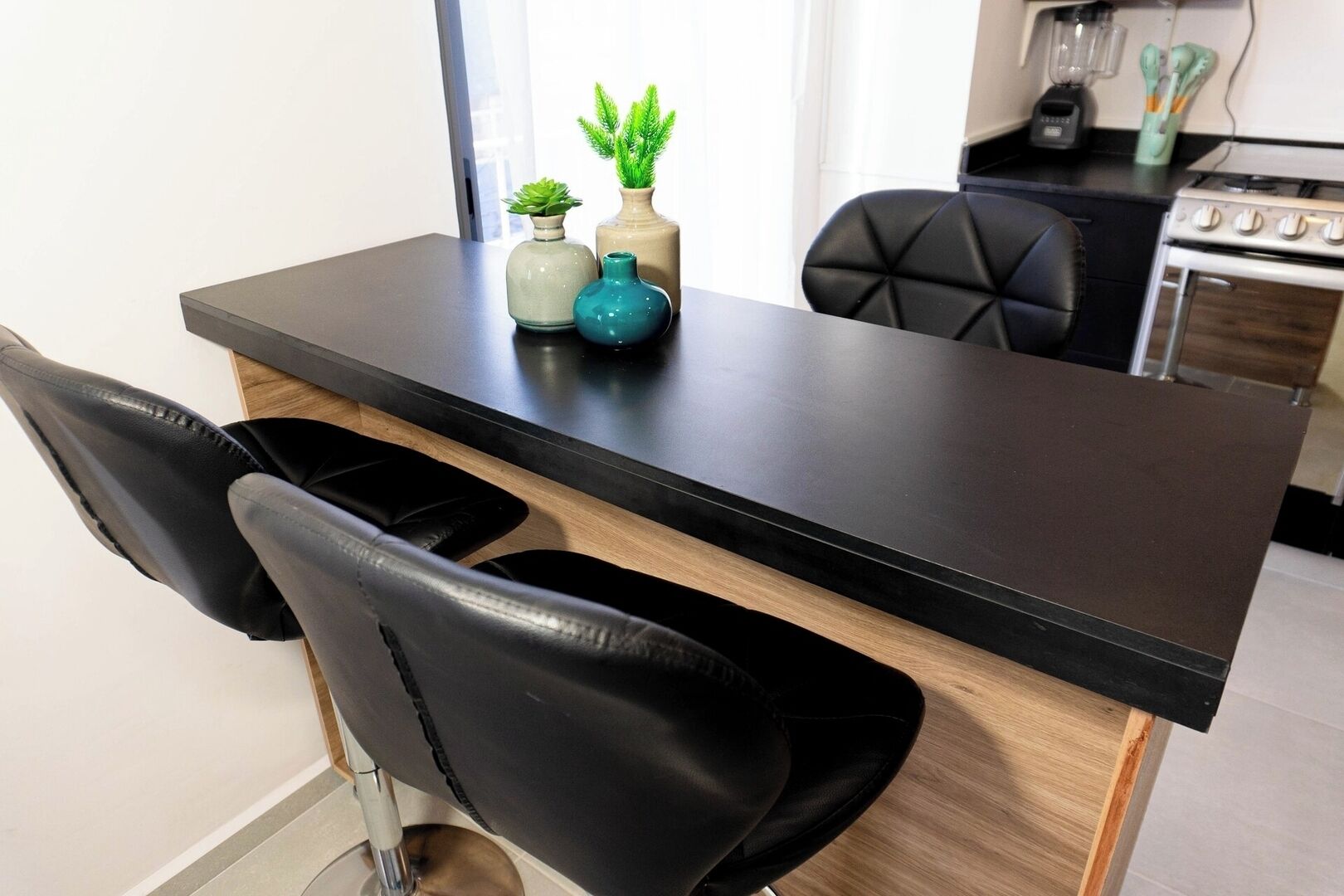 A modern kitchen with a black countertop, two black chairs, and a small potted plant.