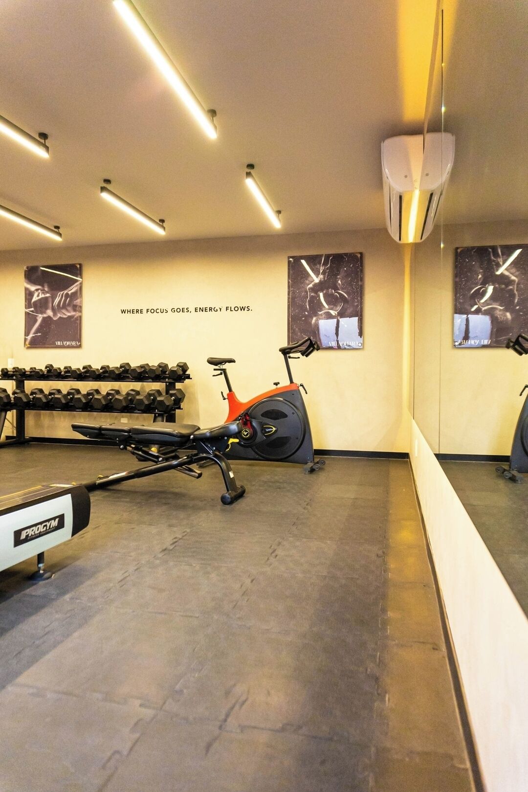 Ein Fitnessraum mit Trainingsgeräten, darunter Hanteln, ein Ergometer und eine Bank.