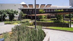 Un edificio moderno con un'area esterna coperta, circondato da giardini curati e un vialetto lastricato.