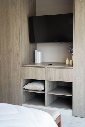 Ein Schlafzimmer mit einem Bett, einem an der Wand befestigten Fernseher und einem Holzschrank mit Einlegeböden.