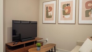 Un soggiorno con una TV a schermo piatto, un tavolino in legno, un divano e tre opere d'arte astratte incorniciate appese al muro.