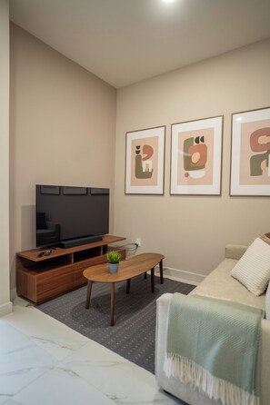 Ein Wohnzimmer mit Flachbildfernseher, Couch, Holz-Couchtisch und drei gerahmten abstrakten Kunstwerken an der Wand.