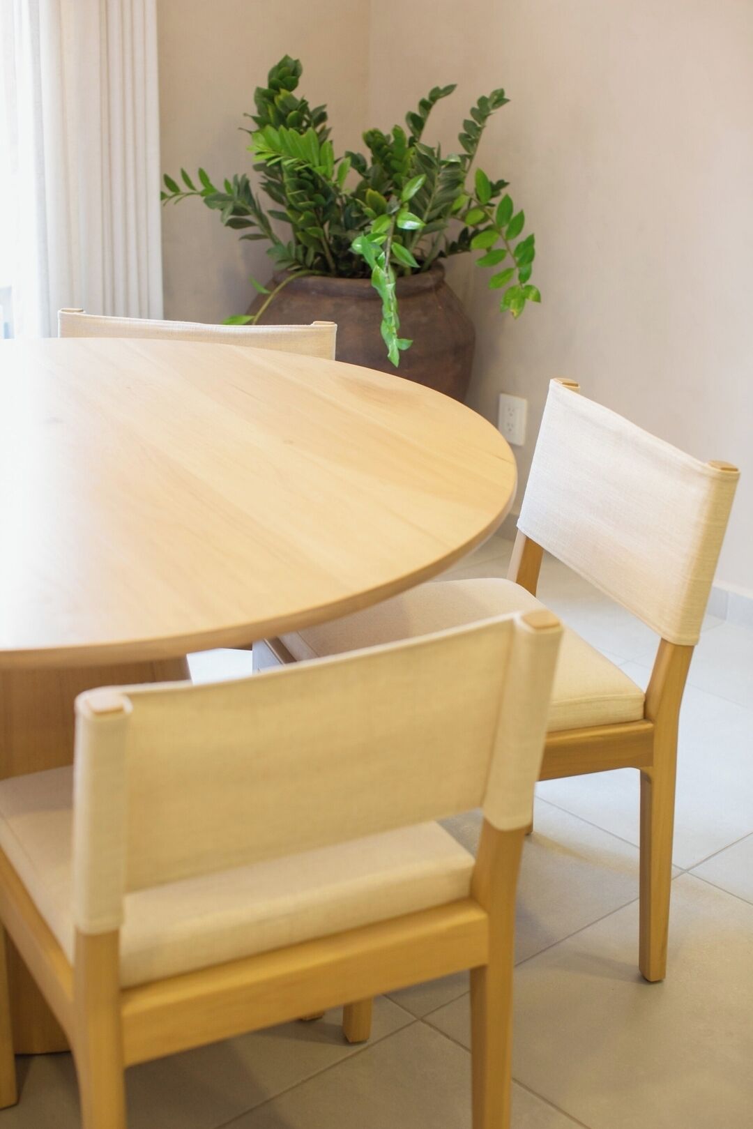 A round wooden table with four chairs, a potted plant, and a light switch on the wall.