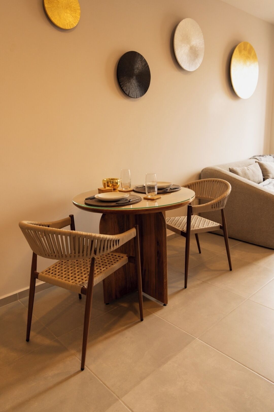 A dining area with a round table, two wicker chairs, and a sofa in the background.