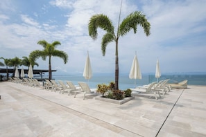 A rooftop lounge area with sun loungers and palm trees, overlooking a body of water. - Mr. W | Stunning 3-Bedroom Apartment in Bantay | Bucerías (Bucerías)