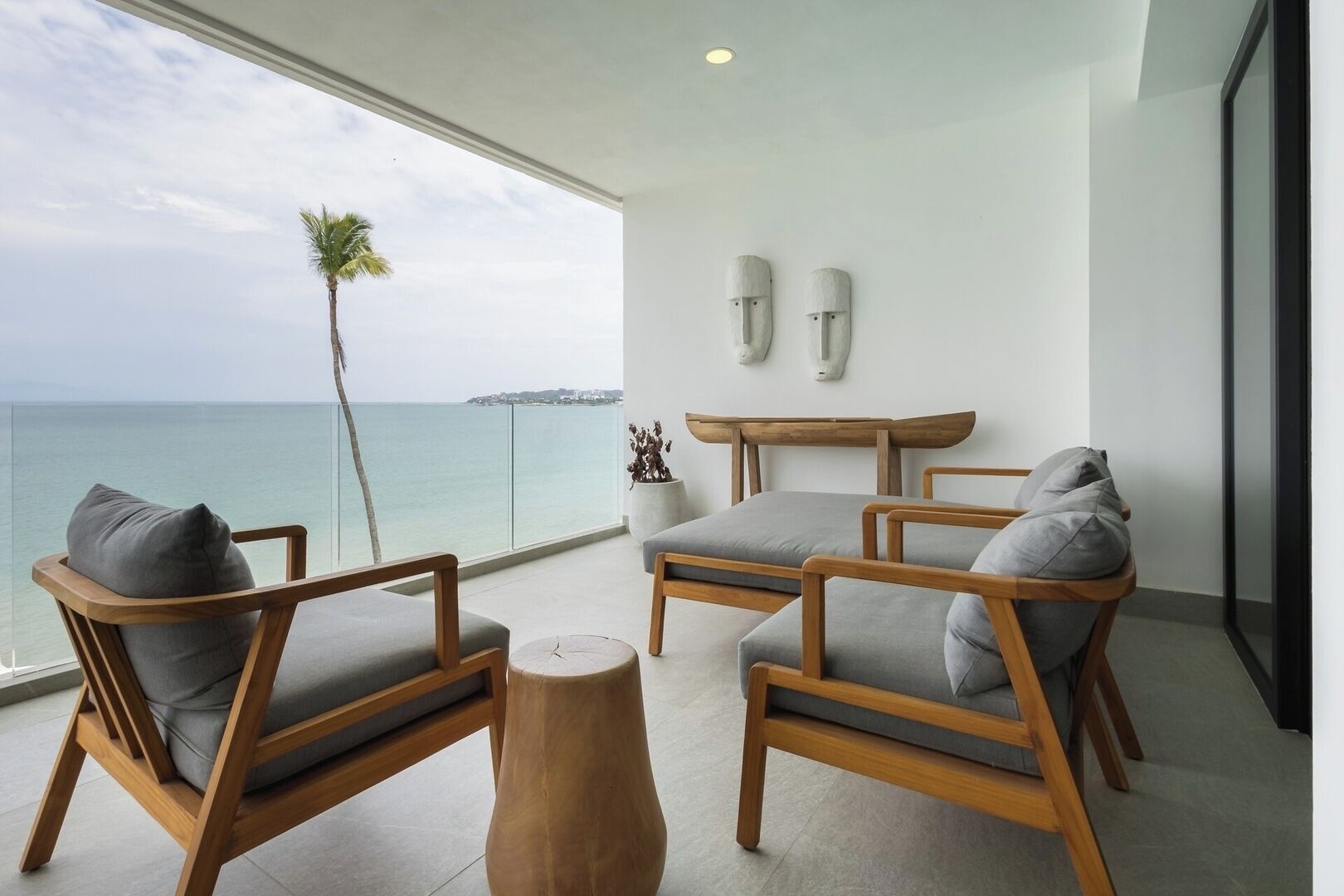 Une chambre moderne avec vue sur la mer, comprenant deux chaises en bois avec des coussins gris, une petite table en bois et une plante décorative.