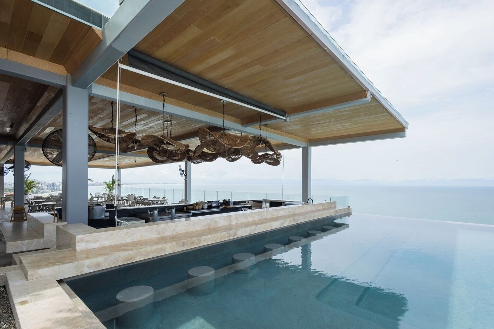 Ein Infinity-Pool mit Barbereich und Sitzgelegenheiten mit Blick auf ein Gewässer.