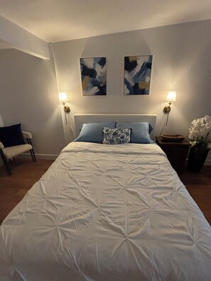 Ein Schlafzimmer mit einem großen Bett, zwei Wandlampen, einem Sessel und abstrakter Kunst an der Wand.