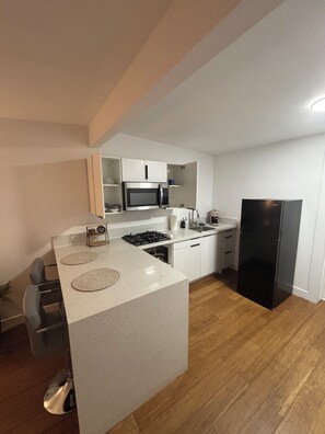 Una cocina moderna con una isla central, muebles blancos, un refrigerador negro y un lavamanos de acero inoxidable.
