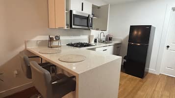 Una cocina moderna con una isla central, taburetes de bar, microondas, estufa y refrigerador.