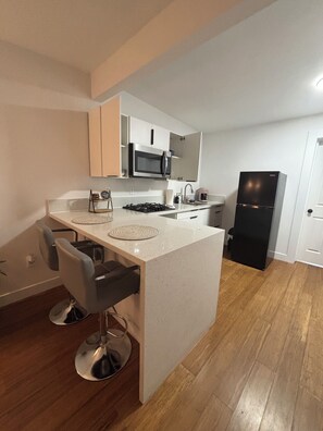 Una cocina moderna con una isla central, taburetes de bar, microondas, estufa y refrigerador.