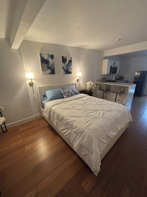 Un dormitorio con cama, lámparas de noche, una mesita de noche y una pequeña mesa con un jarrón de flores.